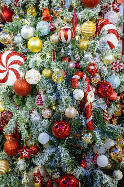 Süslü Noel ağacı, kırmızı, altın ve gümüş takılar, şeker kamışları ve süslü heykelcikler de dahil olmak üzere canlı süslemelerle süslenmiş. Donmuş dallar ve ılık peri ışıklarıyla çevrili, neşeli bir bayram ortamı yaratıyor..