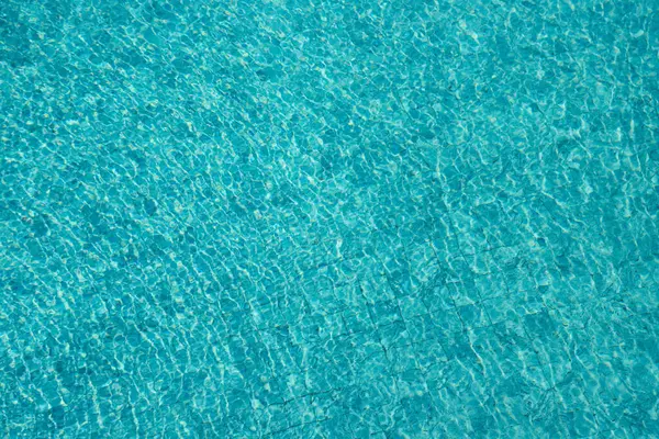 Parıldayan yansımaları ve güneş ışığı altında dalgalanmaları olan canlı mavi su yüzeyi.