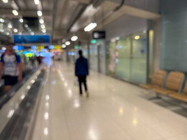 Havaalanı terminali boyunca yürüyen bir yürüyüş yolu ve modern mimari detaylarla yürüyen gezginlerin bulanık görüntüsü.
