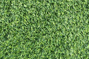 yemyeşil suni bir çimenliğe yakın çekim. Çimenlerin sentetik yaprakları mükemmel bir şekilde hizalanmış ve halı benzeri bir arka plan oluşturuyor.