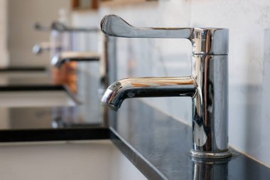 Pürüzsüz krom musluk cilalanmış siyah mermer tezgahın üzerine kurulmuş, arka planda bulanık beyaz mermer arkaplanı var.