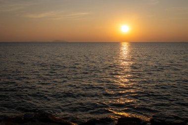 Güneşin suyun yüzeyine sıcacık bir altın yansımasıyla okyanus üzerindeki huzurlu günbatımı manzarası.