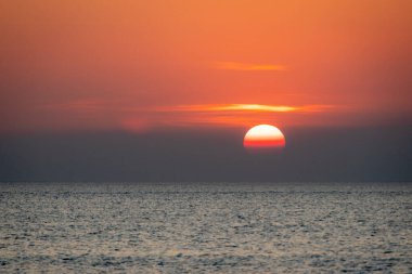 Sakin bir günbatımı sahnesi ufkun altında yavaşça kayboluyor, sakin okyanusun üzerine yumuşak, pembe ve turuncu renkler döküyor..