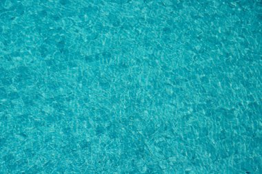 Parıldayan yansımaları ve güneş ışığı altında dalgalanmaları olan canlı mavi su yüzeyi.