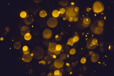 Koyu bir arka planda farklı boyut ve renklerde odanmamış altın bokeh ışıkları.
