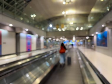 Havaalanı terminali boyunca yürüyen bir yürüyüş yolu ve modern mimari detaylarla yürüyen gezginlerin bulanık görüntüsü.