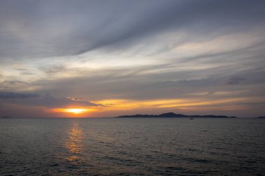 Güneş ufkun altına batıyor, sakin denizin üzerine altın bir parıltı saçıyor. Yalnız bir yelkenli körfez boyunca huzur içinde süzülürken hafif bir esinti suyu dalgalandırır. Martılar tepeden ağlar, sakin atmosferi artırır..