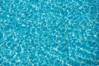 Işıldayan mavi su yüzeyine yakın çekim. Karmaşık ışık yansımaları dinamik dalgalanmalar yaratıyor. Ferahlatıcı ve yazlık bir ortam yaratıyor..