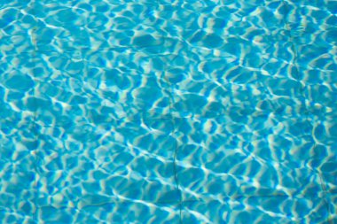 Işıldayan mavi su yüzeyine yakın çekim. Karmaşık ışık yansımaları dinamik dalgalanmalar yaratıyor. Ferahlatıcı ve yazlık bir ortam yaratıyor..