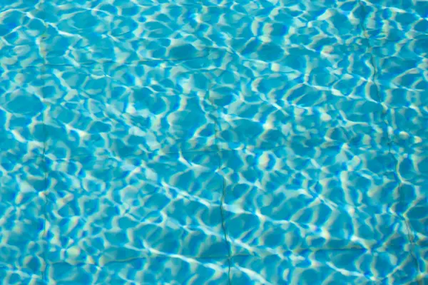 Işıldayan mavi su yüzeyine yakın çekim. Karmaşık ışık yansımaları dinamik dalgalanmalar yaratıyor. Ferahlatıcı ve yazlık bir ortam yaratıyor..