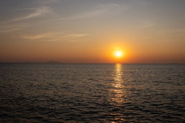 Güneşin suyun yüzeyine sıcacık bir altın yansımasıyla okyanus üzerindeki huzurlu günbatımı manzarası.