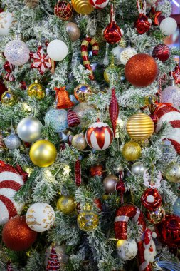 Süslü Noel ağacı, kırmızı, altın ve gümüş takılar, şeker kamışları ve süslü heykelcikler de dahil olmak üzere canlı süslemelerle süslenmiş. Donmuş dallar ve ılık peri ışıklarıyla çevrili, neşeli bir bayram ortamı yaratıyor..