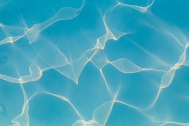 Parlak güneş ışığı yansımalarıyla canlı mavi yüzme havuzu suyunun yakın çekimi dinamik desenler oluşturur.