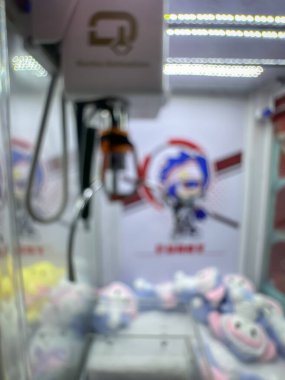Pembe pelüş oyuncaklarla dolu renkli bir pençe makinesi oyuncuları eğlenceli bir oyun salonunda şanslarını denemeye davet ediyor..