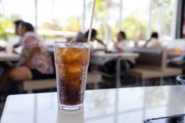 Bir bardak buz gibi kola masanın üzerinde duruyor, yoğunlaşma camda parlıyor. Köpükler davetkar bir şekilde köpürüyor, ferahlatıcı bir içecek vaat ediyor..