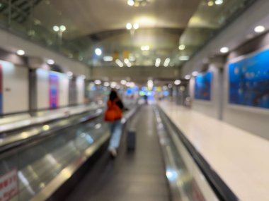 Havaalanı terminali boyunca yürüyen bir yürüyüş yolu ve modern mimari detaylarla yürüyen gezginlerin bulanık görüntüsü.