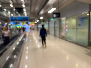 Havaalanı terminali boyunca yürüyen bir yürüyüş yolu ve modern mimari detaylarla yürüyen gezginlerin bulanık görüntüsü.
