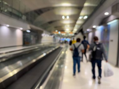 Havaalanı terminali boyunca yürüyen bir yürüyüş yolu ve modern mimari detaylarla yürüyen gezginlerin bulanık görüntüsü.