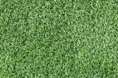 yemyeşil suni bir çimenliğe yakın çekim. Çimenlerin sentetik yaprakları mükemmel bir şekilde hizalanmış ve halı benzeri bir arka plan oluşturuyor.