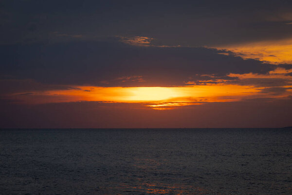 The sun dips below the horizon, casting a golden glow over the calm sea. A gentle breeze ruffles the water as a lone sailboat glides peacefully across the bay. Seagulls cry overhead, adding to the tranquil atmosphere.
