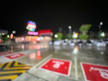 Geceleri bir marketin park alanının bulanık görüntüsü, parlak ışıklı park alanları ve aydınlatılmış mağaza tabelaları.