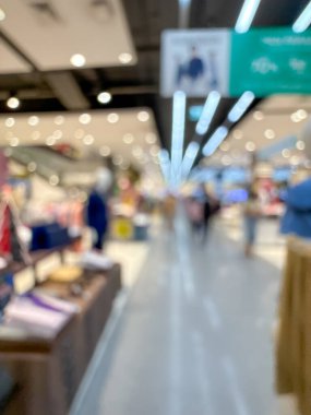 Bir alışveriş merkezi koridorunun bulanık görüntüsü, modern bir perakende ortamın canlı atmosferini gözler önüne seriyor. İnsanlar çeşitli mağazalara girip çıkarken görülüyorlar.