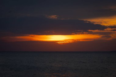 Güneş ufkun altına batıyor, sakin denizin üzerine altın bir parıltı saçıyor. Yalnız bir yelkenli körfez boyunca huzur içinde süzülürken hafif bir esinti suyu dalgalandırır. Martılar tepeden ağlar, sakin atmosferi artırır..