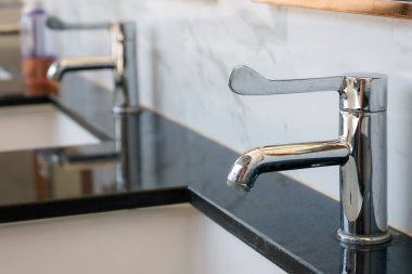 Pürüzsüz krom musluk cilalanmış siyah mermer tezgahın üzerine kurulmuş, arka planda bulanık beyaz mermer arkaplanı var.