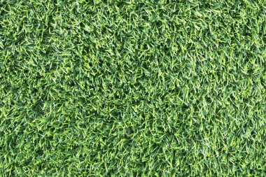 yemyeşil suni bir çimenliğe yakın çekim. Çimenlerin sentetik yaprakları mükemmel bir şekilde hizalanmış ve halı benzeri bir arka plan oluşturuyor.