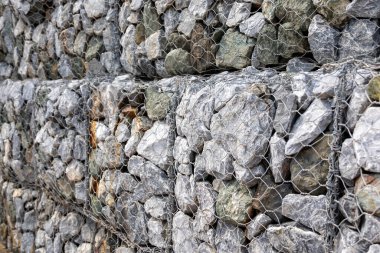 Gabion duvar, gri taşların ve tel örgülerin dokusunu gösteriyor. Görüntü, inşaat malzemesinin ayrıntılı yapısını ve dayanıklı yapısını vurguluyor..