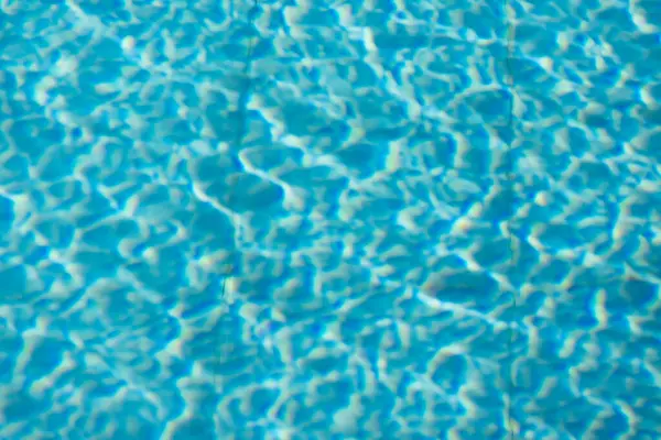 Işıldayan mavi su yüzeyine yakın çekim. Karmaşık ışık yansımaları dinamik dalgalanmalar yaratıyor. Ferahlatıcı ve yazlık bir ortam yaratıyor..