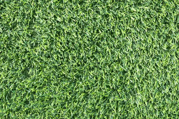 yemyeşil suni bir çimenliğe yakın çekim. Çimenlerin sentetik yaprakları mükemmel bir şekilde hizalanmış ve halı benzeri bir arka plan oluşturuyor.