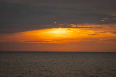 Güneş ufkun altına batıyor, sakin denizin üzerine altın bir parıltı saçıyor. Yalnız bir yelkenli körfez boyunca huzur içinde süzülürken hafif bir esinti suyu dalgalandırır. Martılar tepeden ağlar, sakin atmosferi artırır..