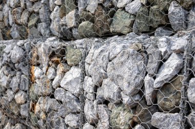 Gabion duvar, gri taşların ve tel örgülerin dokusunu gösteriyor. Görüntü, inşaat malzemesinin ayrıntılı yapısını ve dayanıklı yapısını vurguluyor..