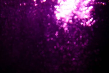 Soyut bulanık mor parıltı dokusu ışıltılı bokeh ışıklarıyla şenlikli bir zemin oluşturuyor.