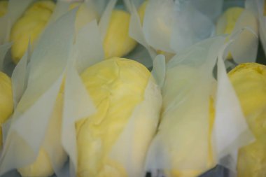 Beyaz kağıda sarılmış taze durian meyveleri, sarı rengini vurgulayan sıcak ışıklarla bir pazarda sergileniyor.