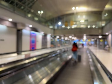 Havaalanı terminali boyunca yürüyen bir yürüyüş yolu ve modern mimari detaylarla yürüyen gezginlerin bulanık görüntüsü.