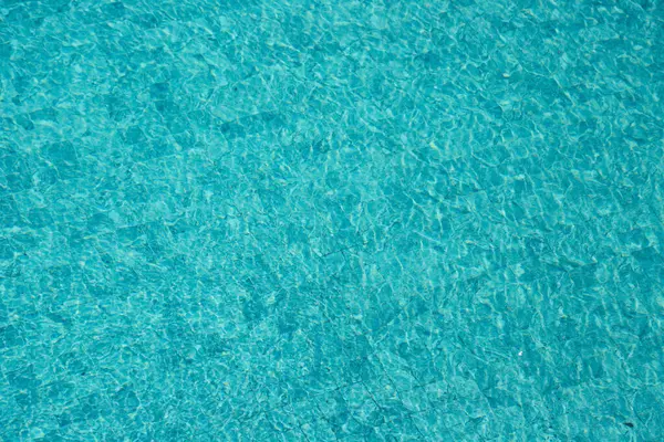 Parıldayan yansımaları ve güneş ışığı altında dalgalanmaları olan canlı mavi su yüzeyi.