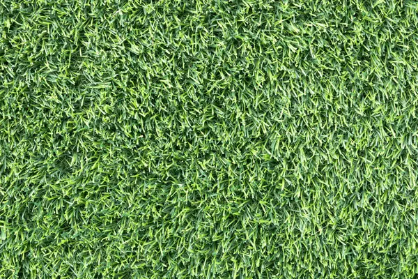 yemyeşil suni bir çimenliğe yakın çekim. Çimenlerin sentetik yaprakları mükemmel bir şekilde hizalanmış ve halı benzeri bir arka plan oluşturuyor.