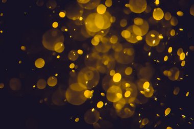 Koyu bir arka planda farklı boyut ve renklerde odanmamış altın bokeh ışıkları.