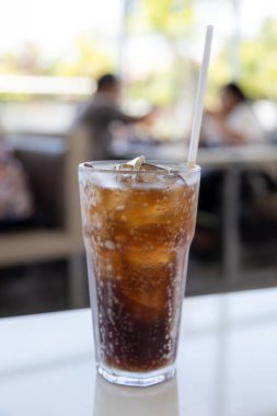 Bir bardak buz gibi kola masanın üzerinde duruyor, yoğunlaşma camda parlıyor. Köpükler davetkar bir şekilde köpürüyor, ferahlatıcı bir içecek vaat ediyor..