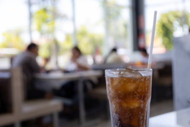 Bir bardak buz gibi kola masanın üzerinde duruyor, yoğunlaşma camda parlıyor. Köpükler davetkar bir şekilde köpürüyor, ferahlatıcı bir içecek vaat ediyor..