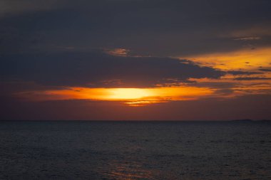 Güneş ufkun altına batıyor, sakin denizin üzerine altın bir parıltı saçıyor. Yalnız bir yelkenli körfez boyunca huzur içinde süzülürken hafif bir esinti suyu dalgalandırır. Martılar tepeden ağlar, sakin atmosferi artırır..