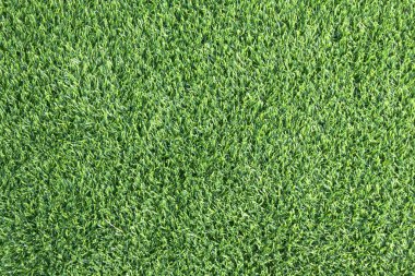 yemyeşil suni bir çimenliğe yakın çekim. Çimenlerin sentetik yaprakları mükemmel bir şekilde hizalanmış ve halı benzeri bir arka plan oluşturuyor.