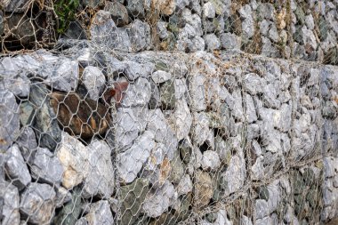 Gabion duvar, gri taşların ve tel örgülerin dokusunu gösteriyor. Görüntü, inşaat malzemesinin ayrıntılı yapısını ve dayanıklı yapısını vurguluyor..