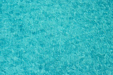 Parıldayan yansımaları ve güneş ışığı altında dalgalanmaları olan canlı mavi su yüzeyi.