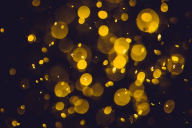Koyu bir arka planda farklı boyut ve renklerde odanmamış altın bokeh ışıkları.