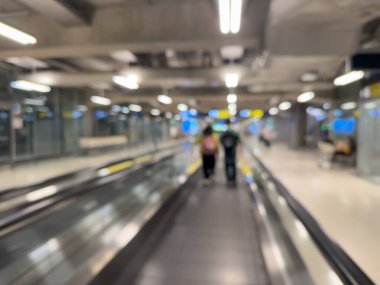 Havaalanı terminali boyunca yürüyen bir yürüyüş yolu ve modern mimari detaylarla yürüyen gezginlerin bulanık görüntüsü.