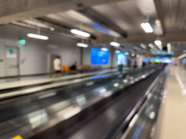 Havaalanı terminali boyunca yürüyen bir yürüyüş yolu ve modern mimari detaylarla yürüyen gezginlerin bulanık görüntüsü.