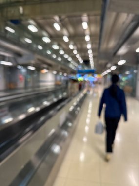 Havaalanı terminali boyunca yürüyen bir yürüyüş yolu ve modern mimari detaylarla yürüyen gezginlerin bulanık görüntüsü.